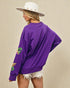 Person wearing a purple sweatshirt with patches on a beige background