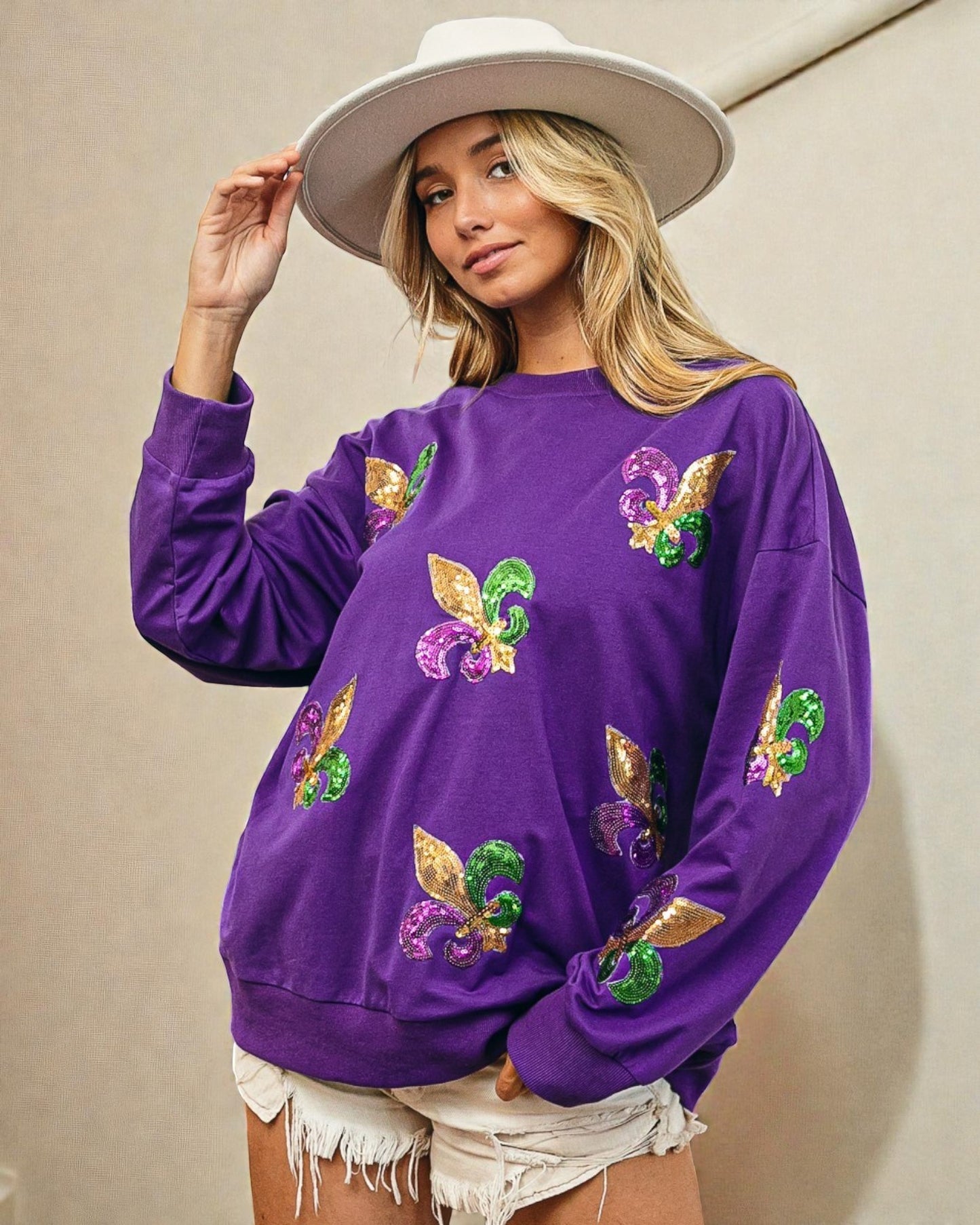 Woman wearing a purple sweatshirt with colorful designs, holding a white hat.