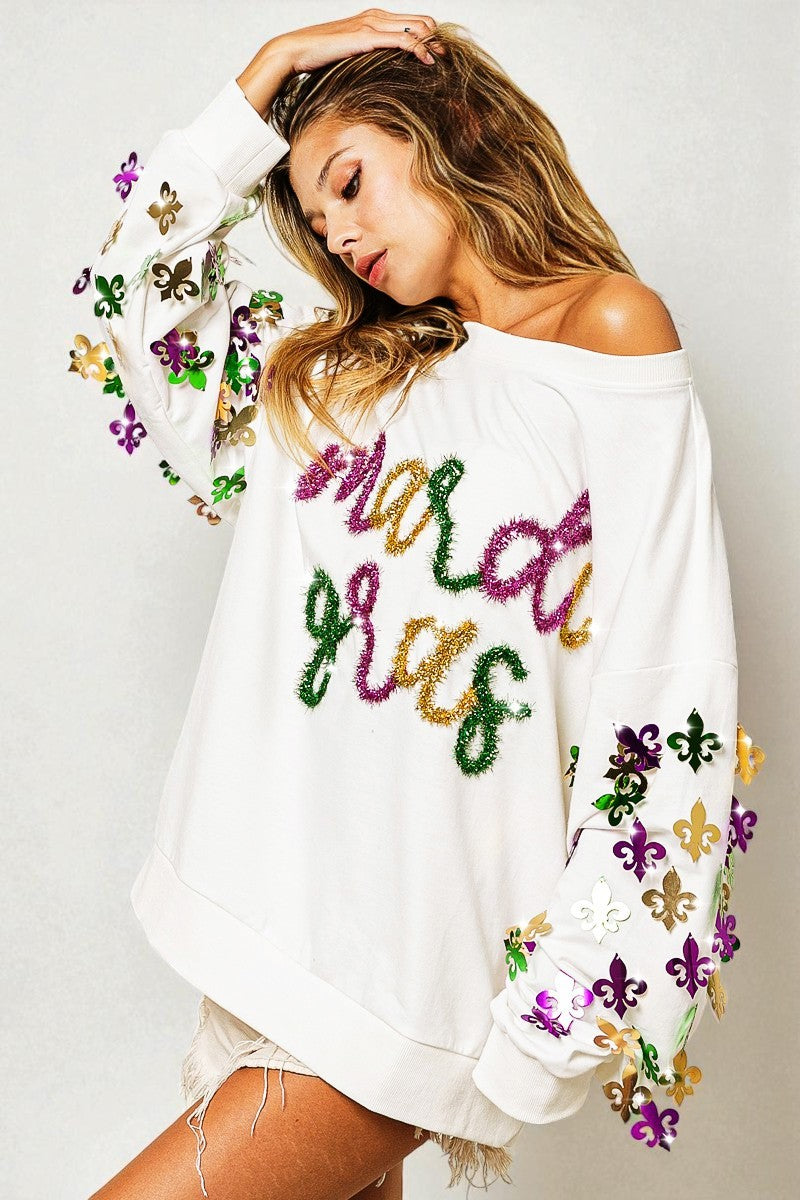 Woman wearing a white off-shoulder sweater with colorful text and patterns on a plain background