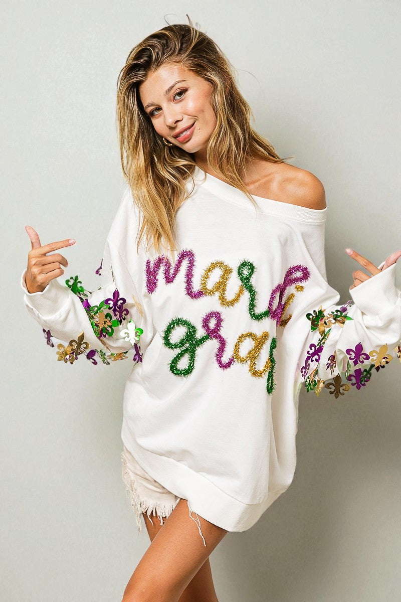 Woman wearing a white off-shoulder sweater with colorful text and patterns on a plain background