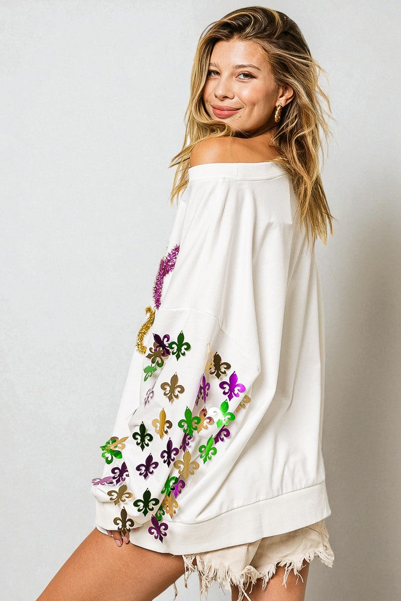 Woman wearing a white off-shoulder top with colorful fleur de lis designs on a plain background