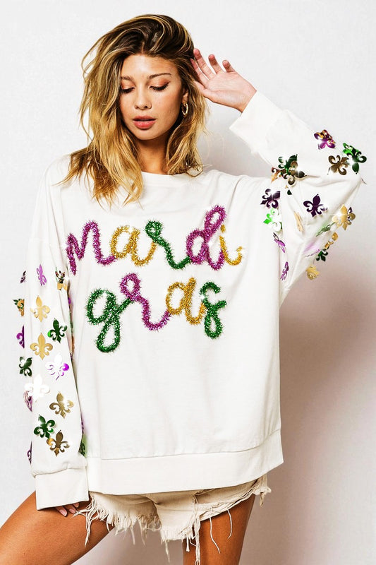 Woman wearing a white sweatshirt with 'Mardi Gras' text and colorful embellishments on a plain background