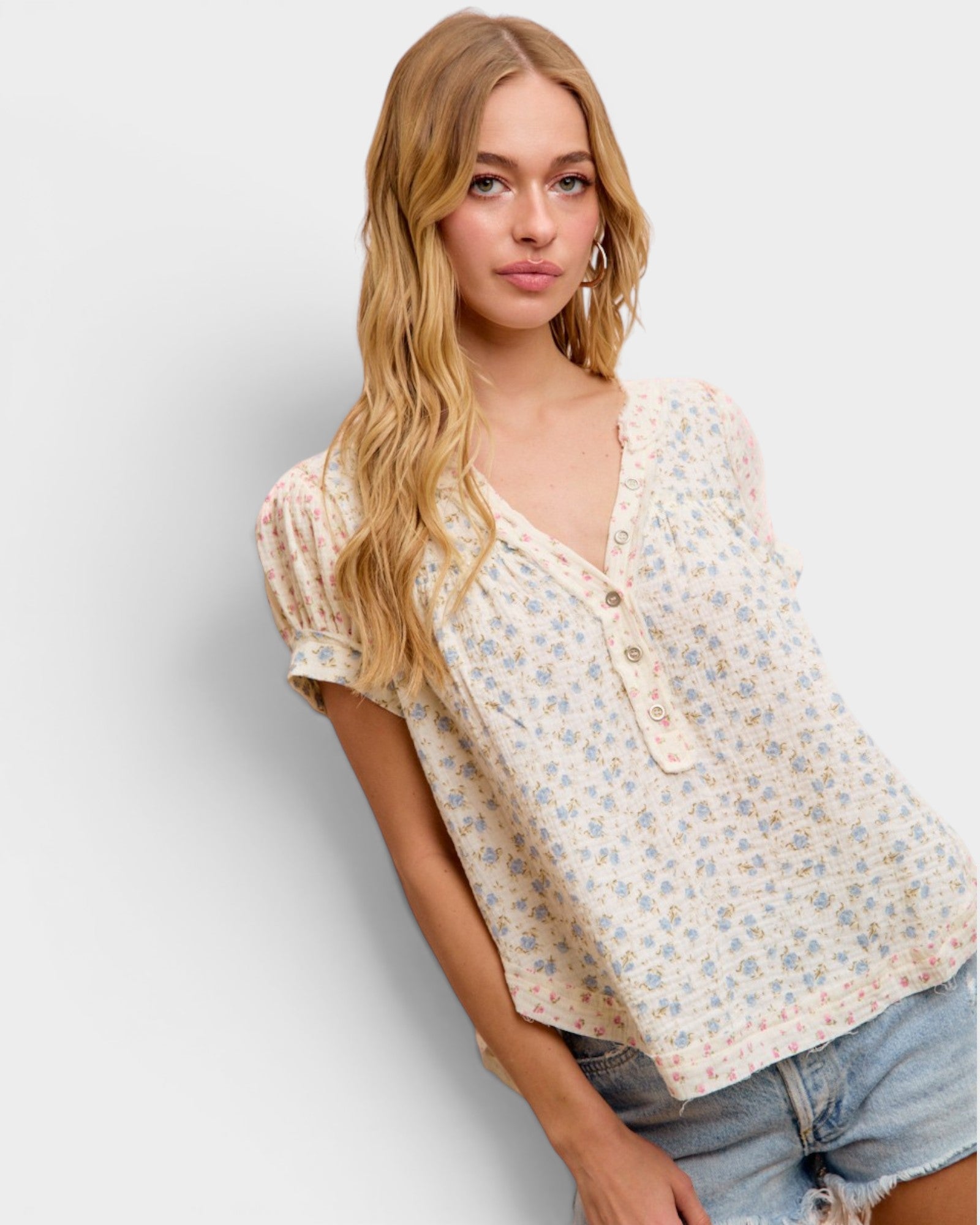 Woman wearing a floral blouse and denim shorts against a plain background