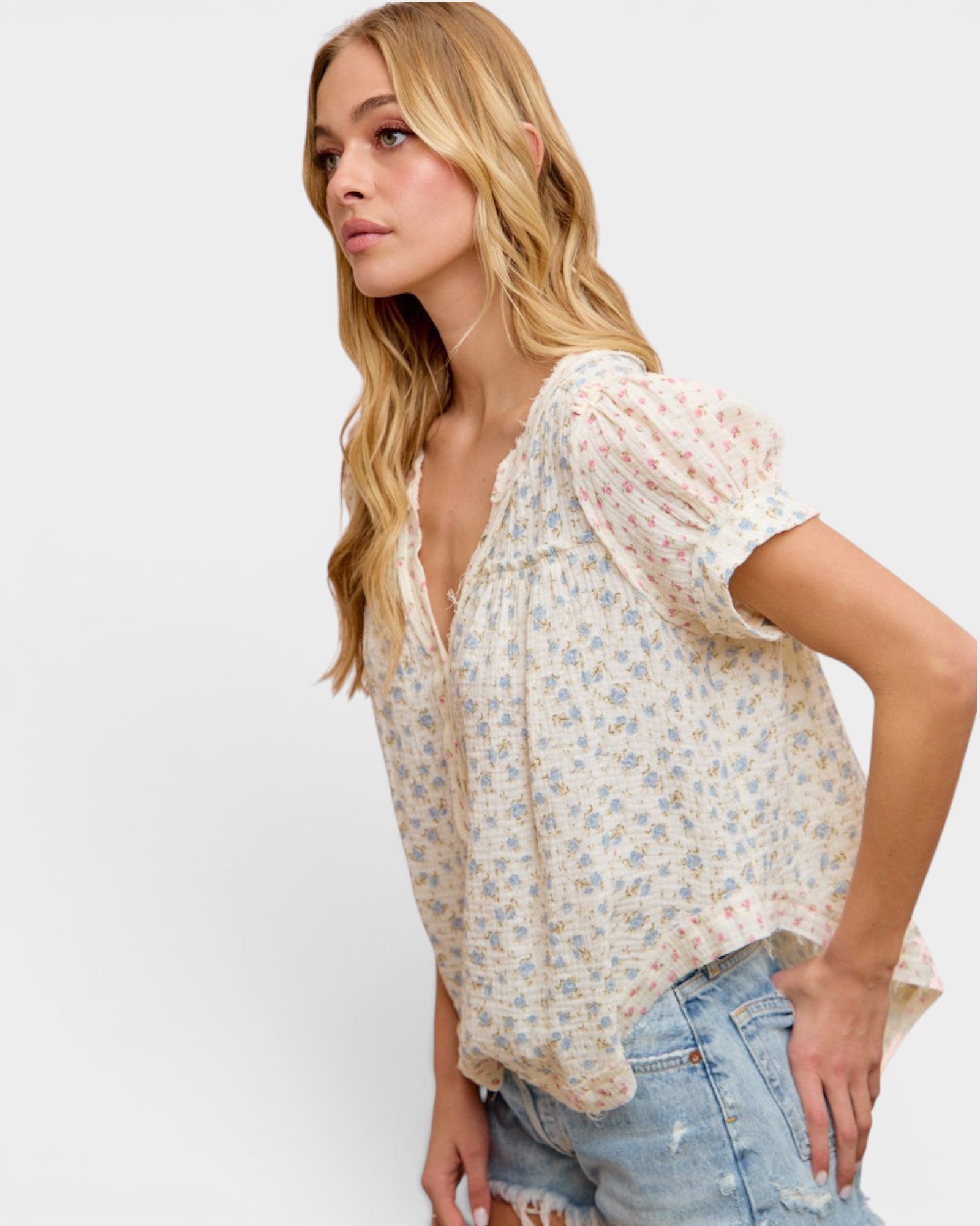 Woman wearing a floral blouse and denim shorts on a white background