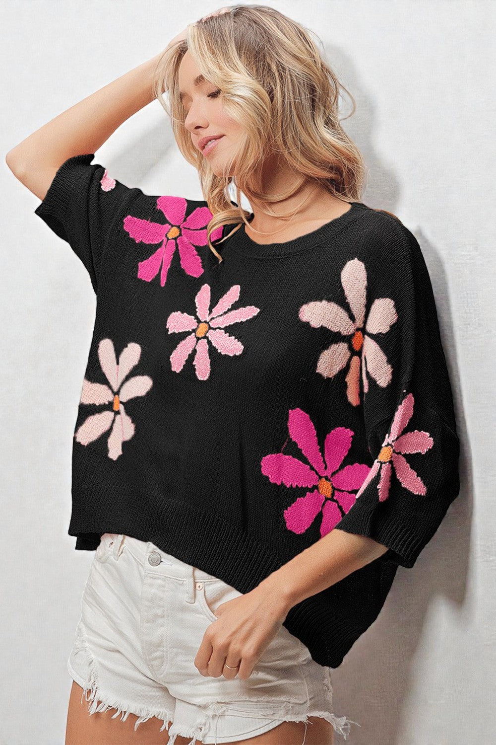 Woman wearing a black sweater with pink floral patterns against a white background