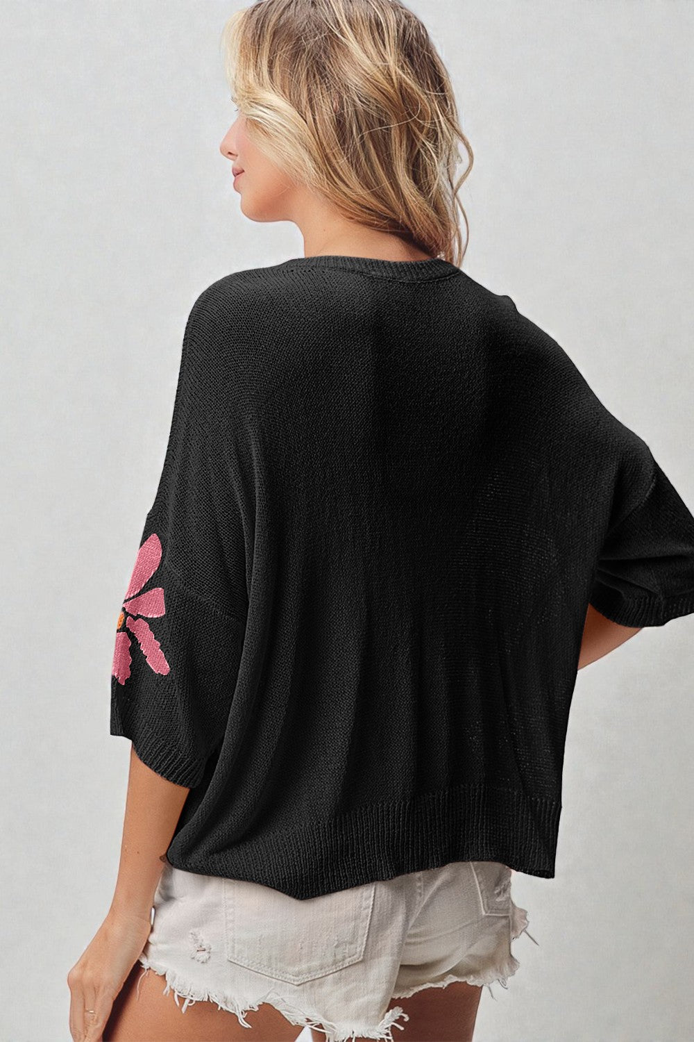 Person wearing a black sweater with a pink floral design on the sleeve against a plain background