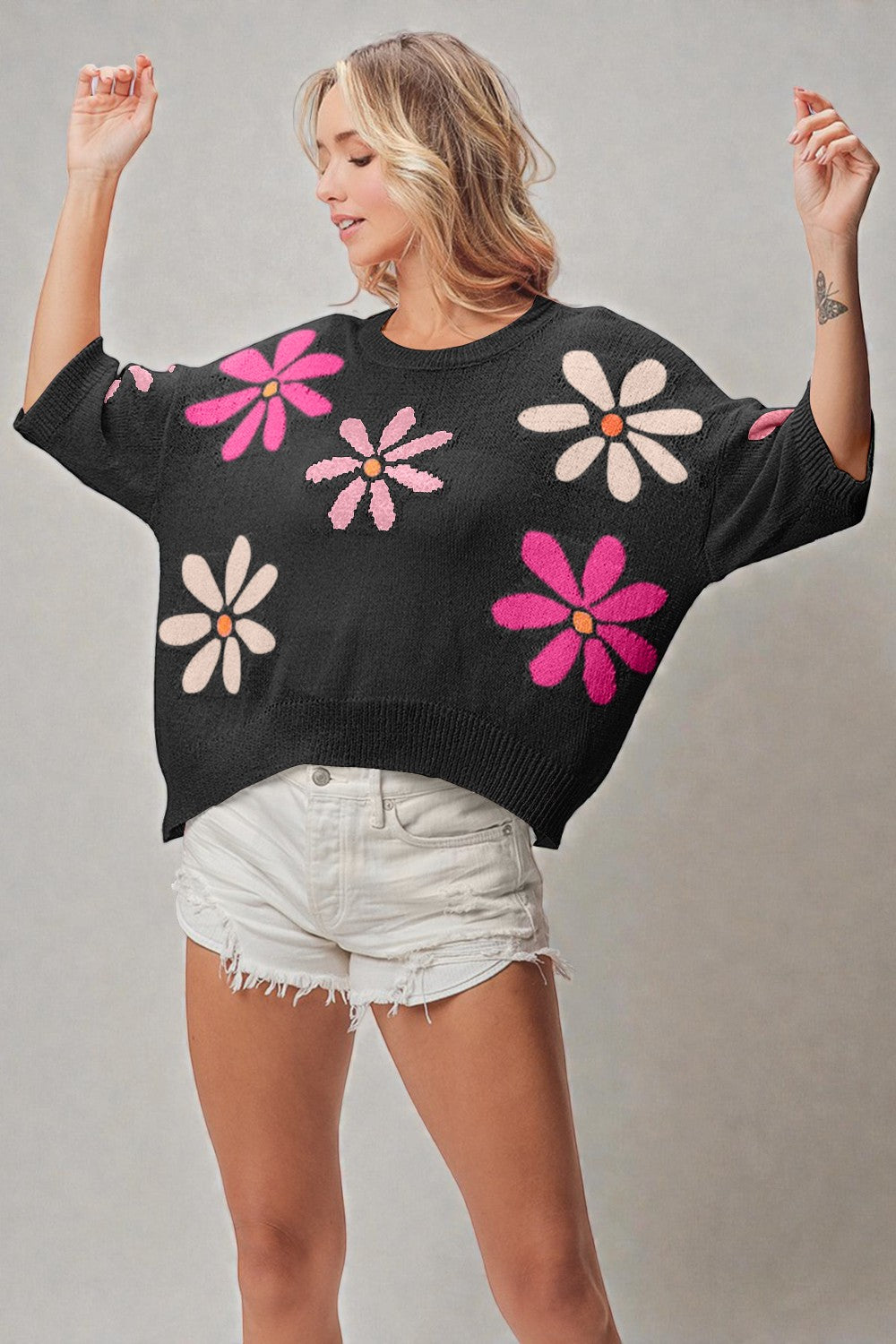 Woman wearing a black sweater with colorful flower patterns on a plain background