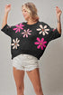Woman wearing a black sweater with colorful flower patterns on a plain background