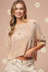 Woman wearing a beige sweater with floral patterns on a pink background