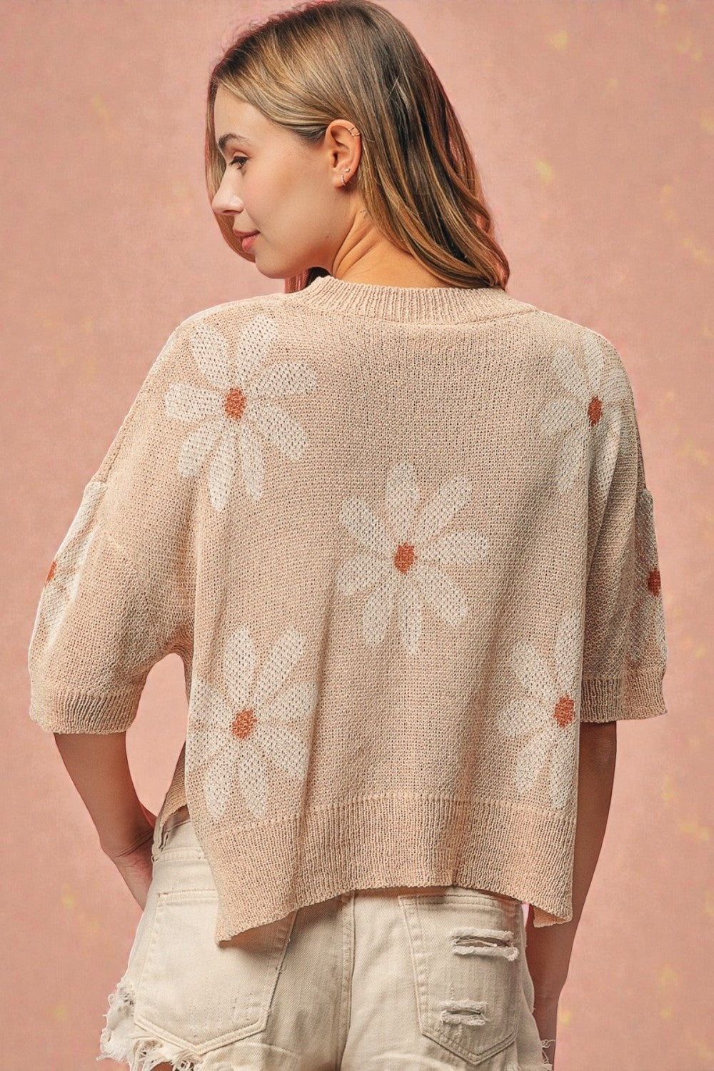 Woman wearing a beige knit cardigan with floral patterns on a pink background