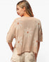 A woman shown from the back wearing a beige knit sweater with large white daisy patterns and tan centers, paired with light beige shorts, against a plain white background.