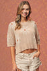 Woman wearing a beige floral knit top and denim shorts against a warm-toned background