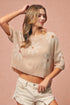 Woman wearing a beige knit top with floral patterns on a pink background
