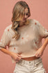 Woman wearing a beige floral knit top against a pink background