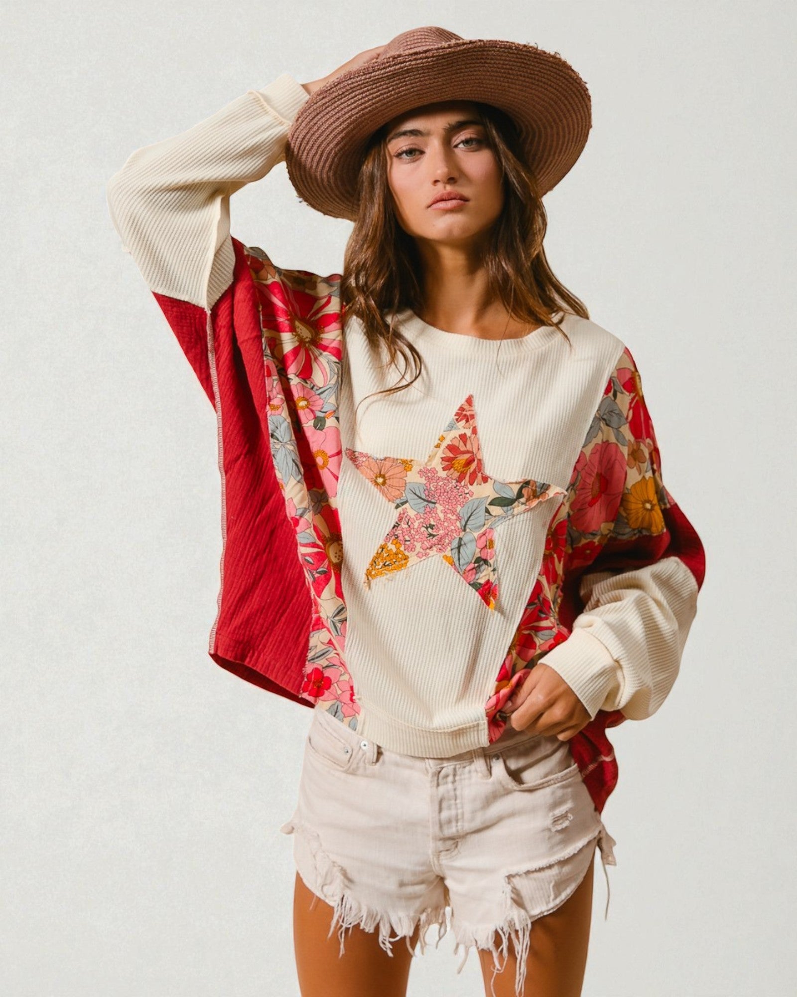 Woman wearing a colorful star-patterned sweatshirt, red jacket, and white shorts on a plain background