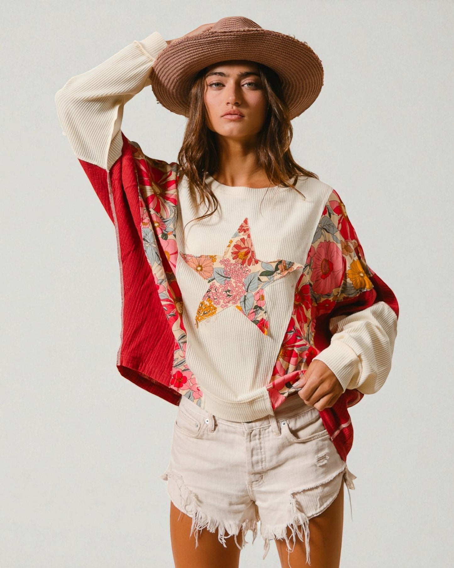 Woman wearing a floral top, red and patterned cardigan, and white shorts on a plain background