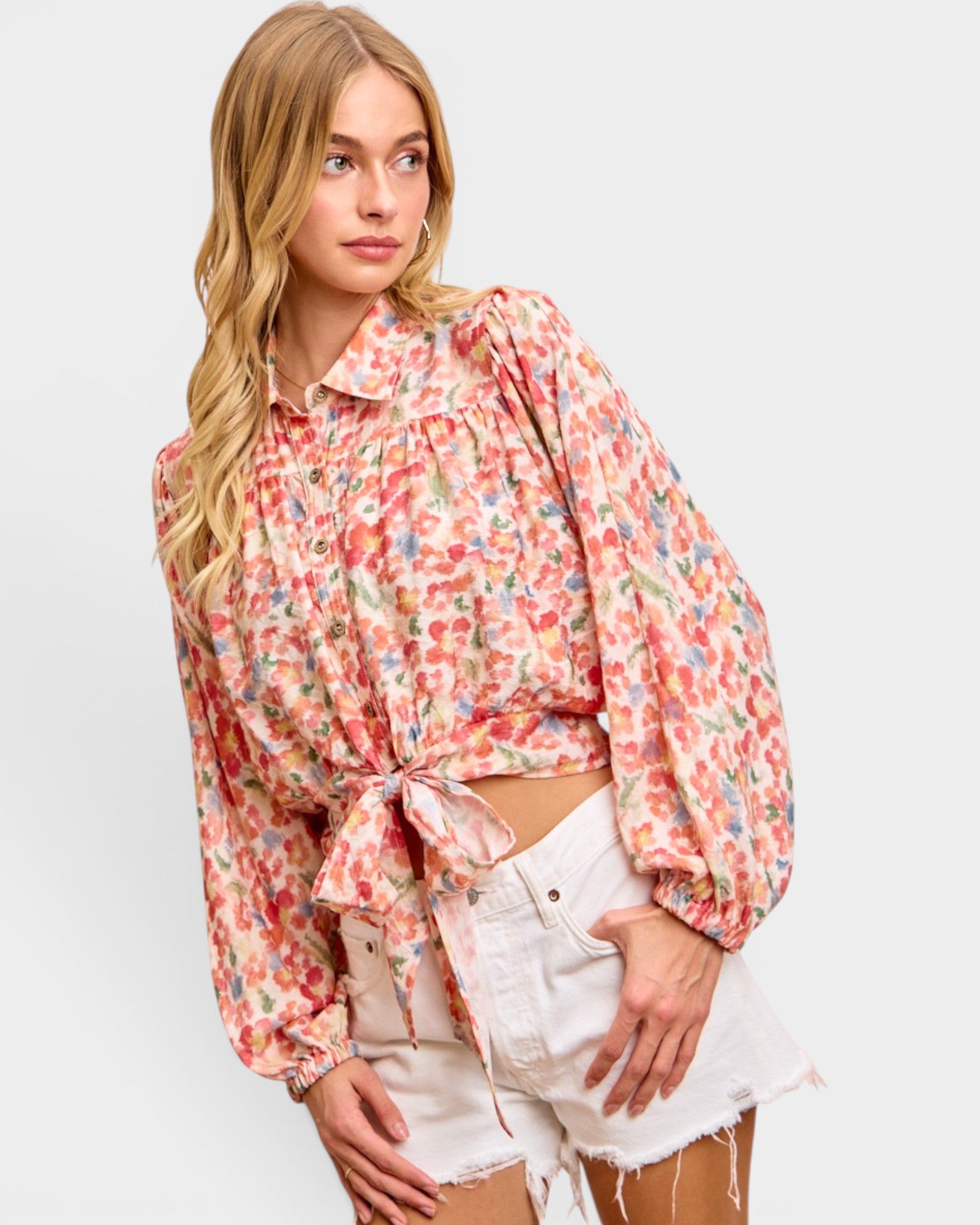 Woman wearing a floral blouse and white shorts on a plain background