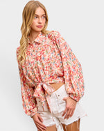 Woman wearing a floral blouse and white shorts on a plain background