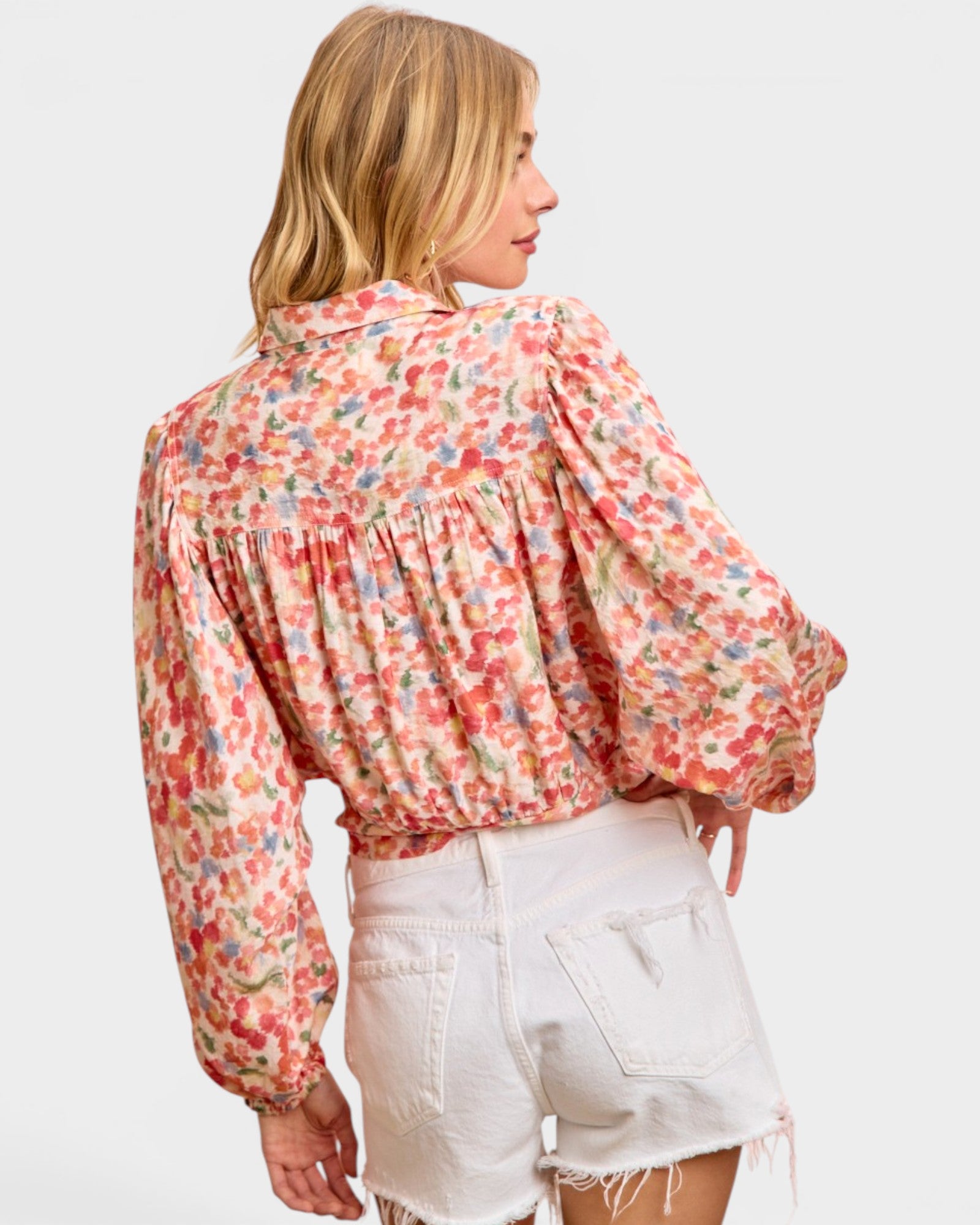 Woman wearing a floral blouse and white shorts on a light gray background