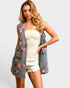 Woman wearing a floral denim vest over a white top and shorts on a plain background