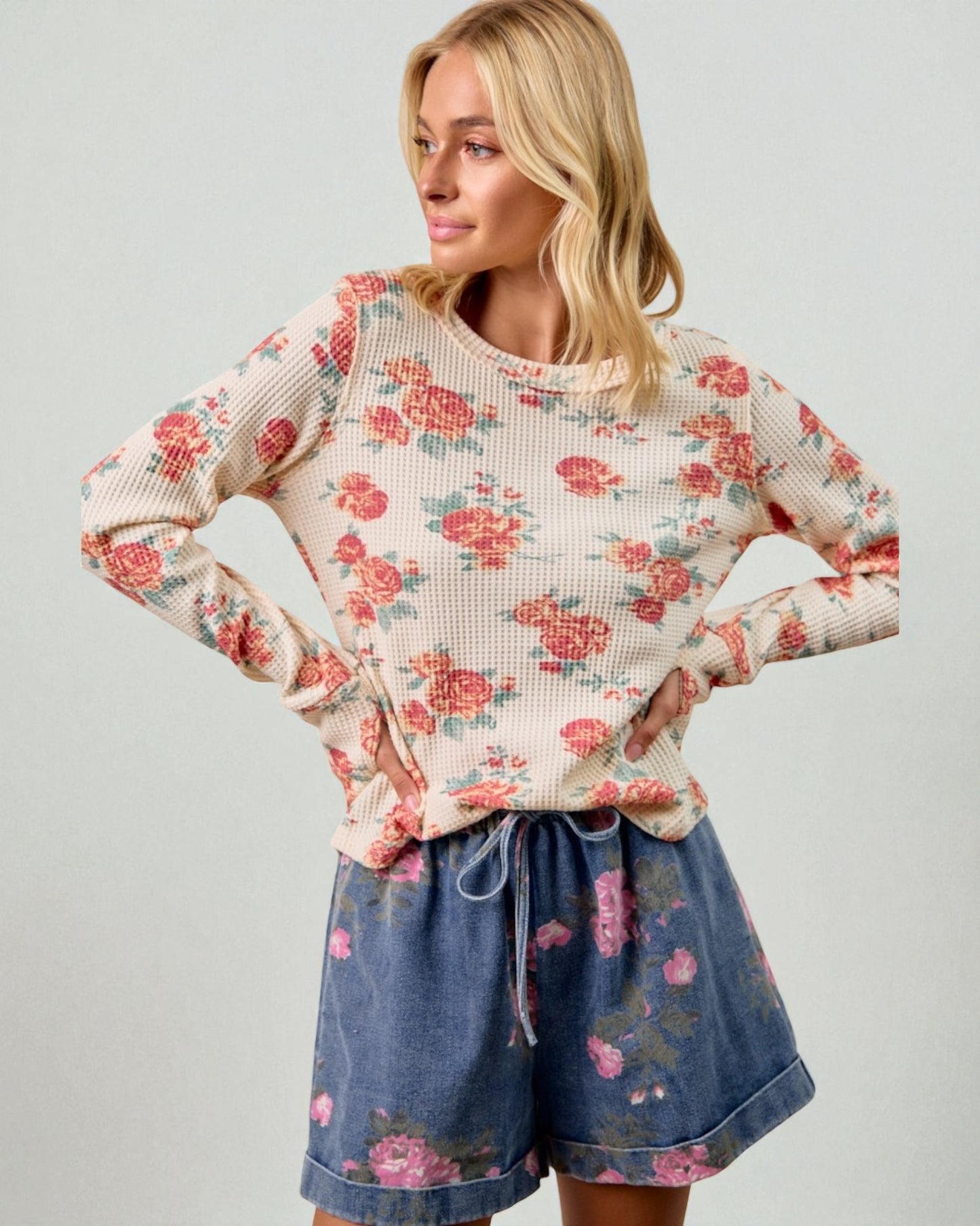 Woman wearing a floral long-sleeve top and denim shorts on a plain background