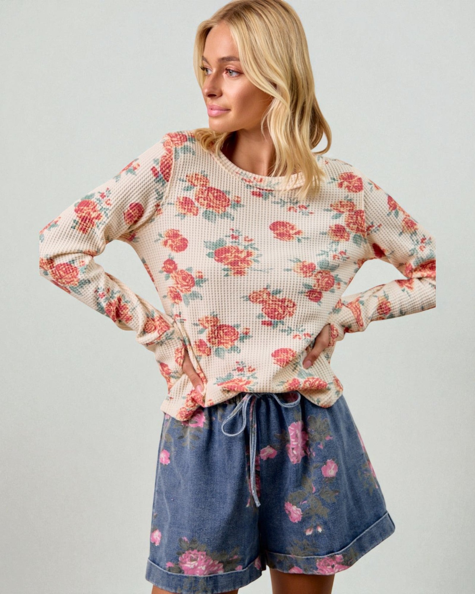 Woman wearing a floral long-sleeve top and denim shorts on a plain background