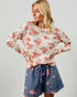 Woman wearing a floral long-sleeve top and denim shorts on a plain background