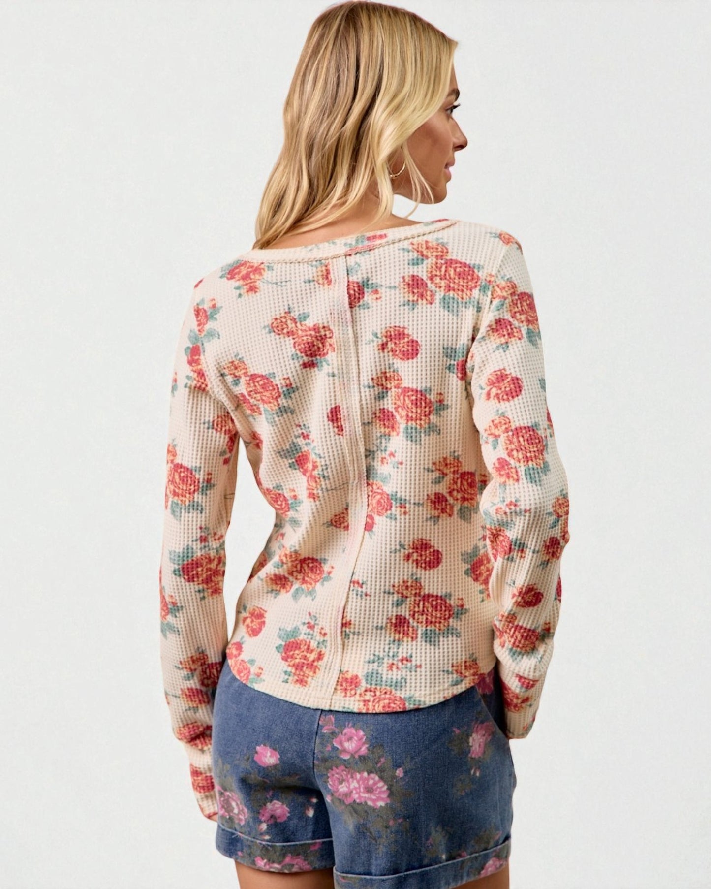 Woman wearing a floral long-sleeve top and denim shorts on a white background