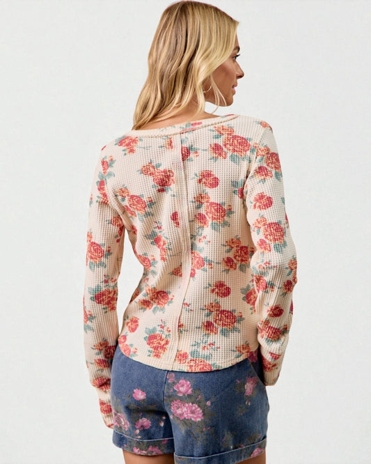 Woman wearing a floral long-sleeve top and denim shorts on a white background