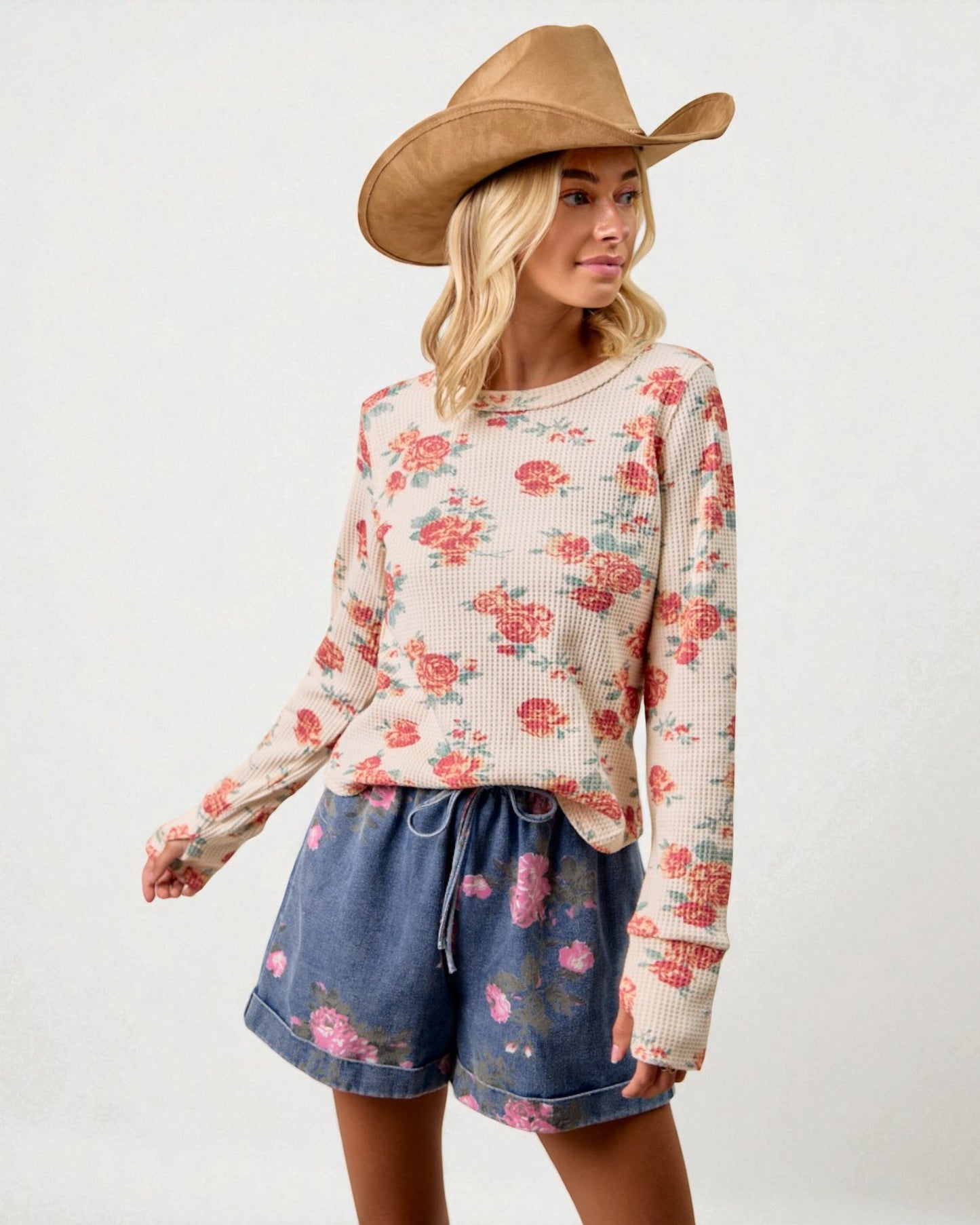 Woman wearing a floral sweater and denim shorts with a cowboy hat on a white background
