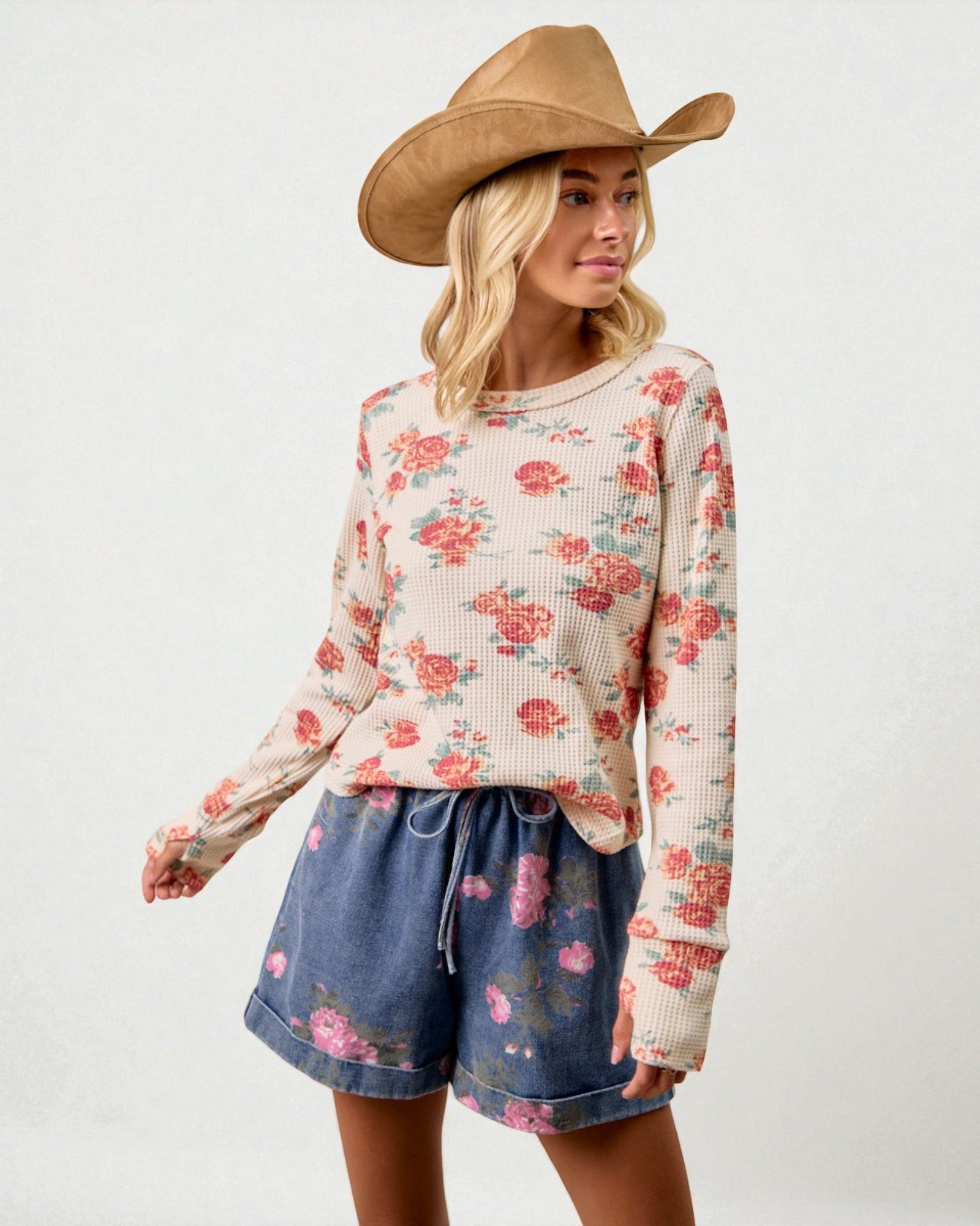 Woman wearing a floral sweater and denim shorts with a cowboy hat on a white background