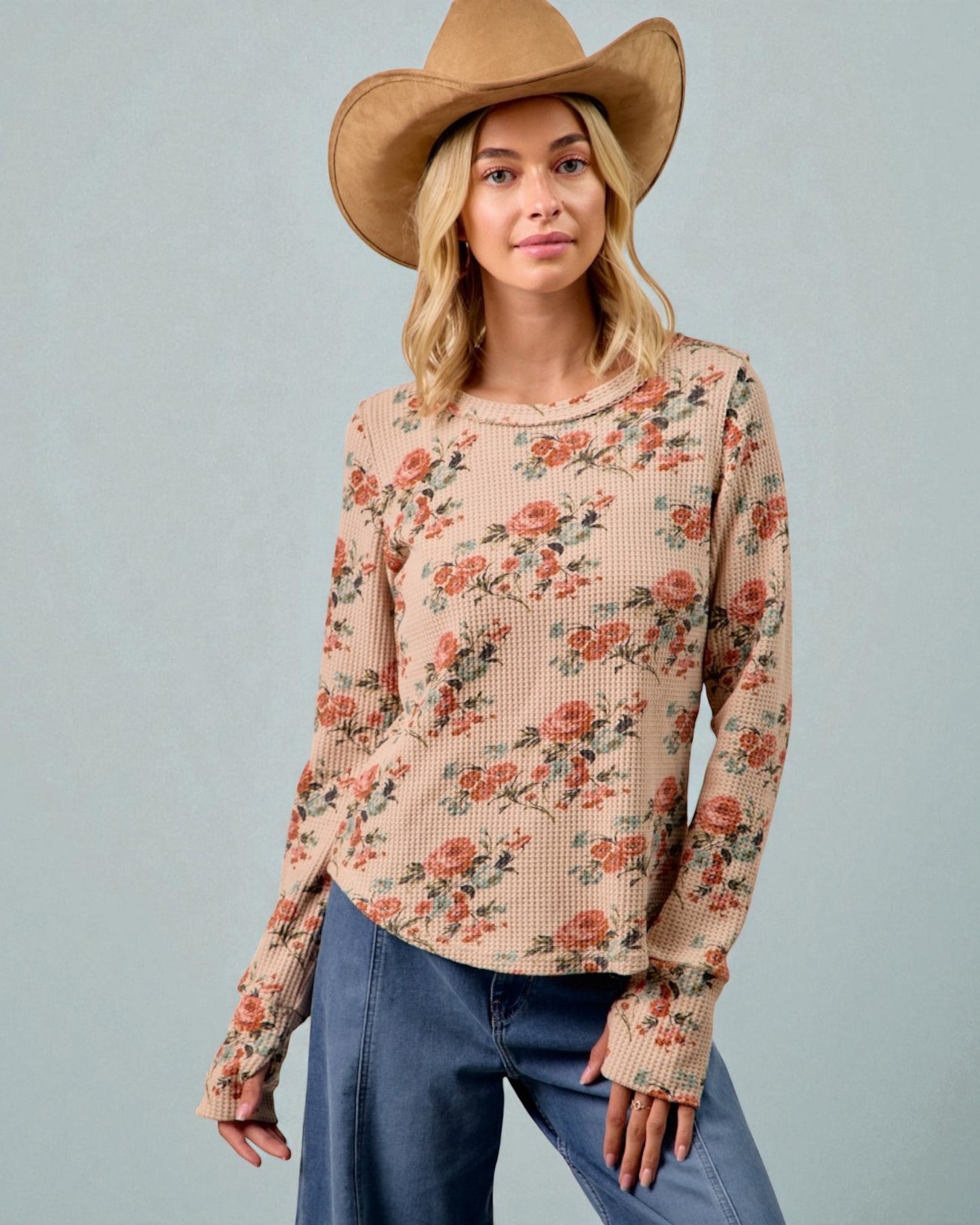 Woman wearing a floral long-sleeve top and wide-brimmed hat against a gray background