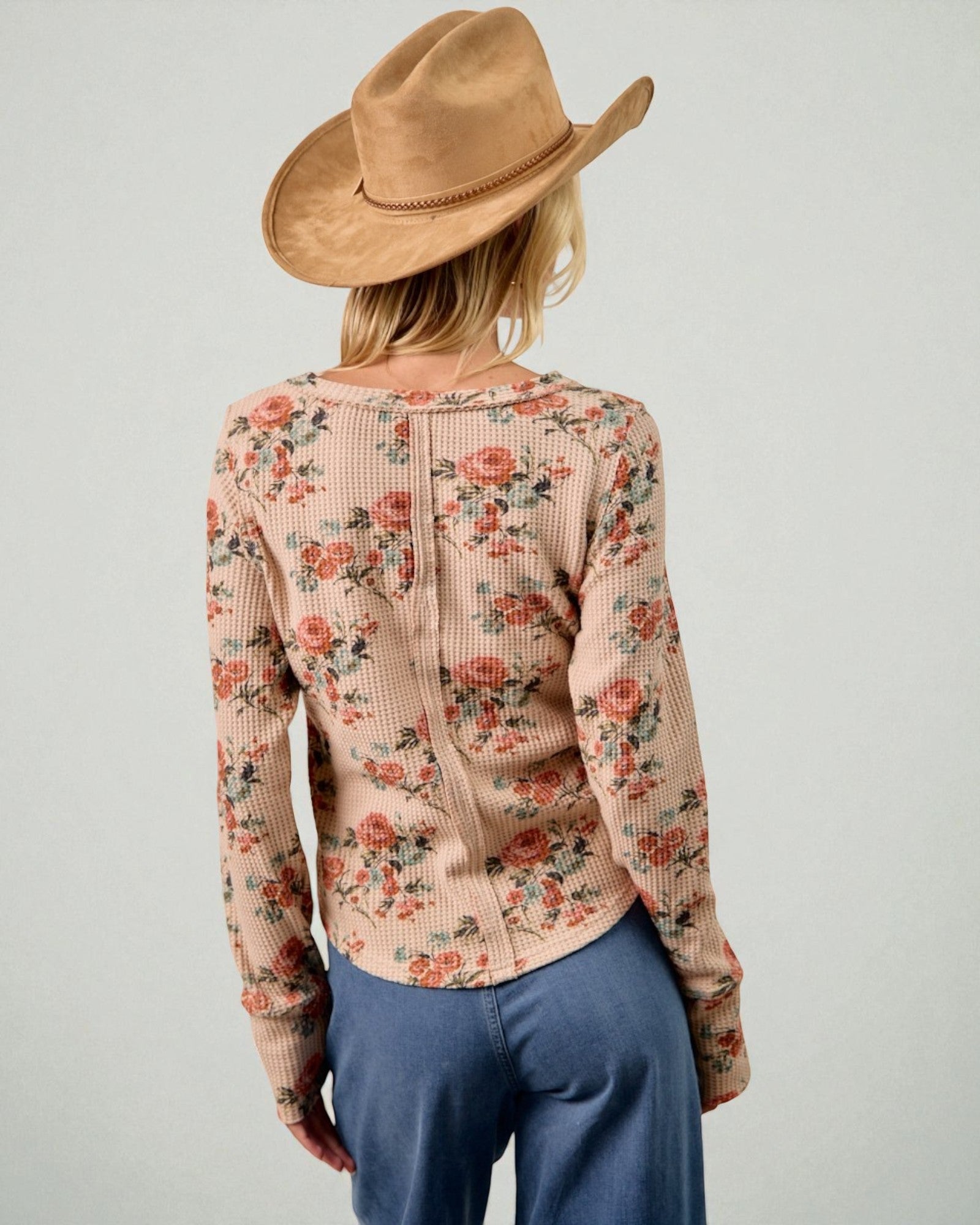 Person wearing a floral sweater and brown hat on a plain background