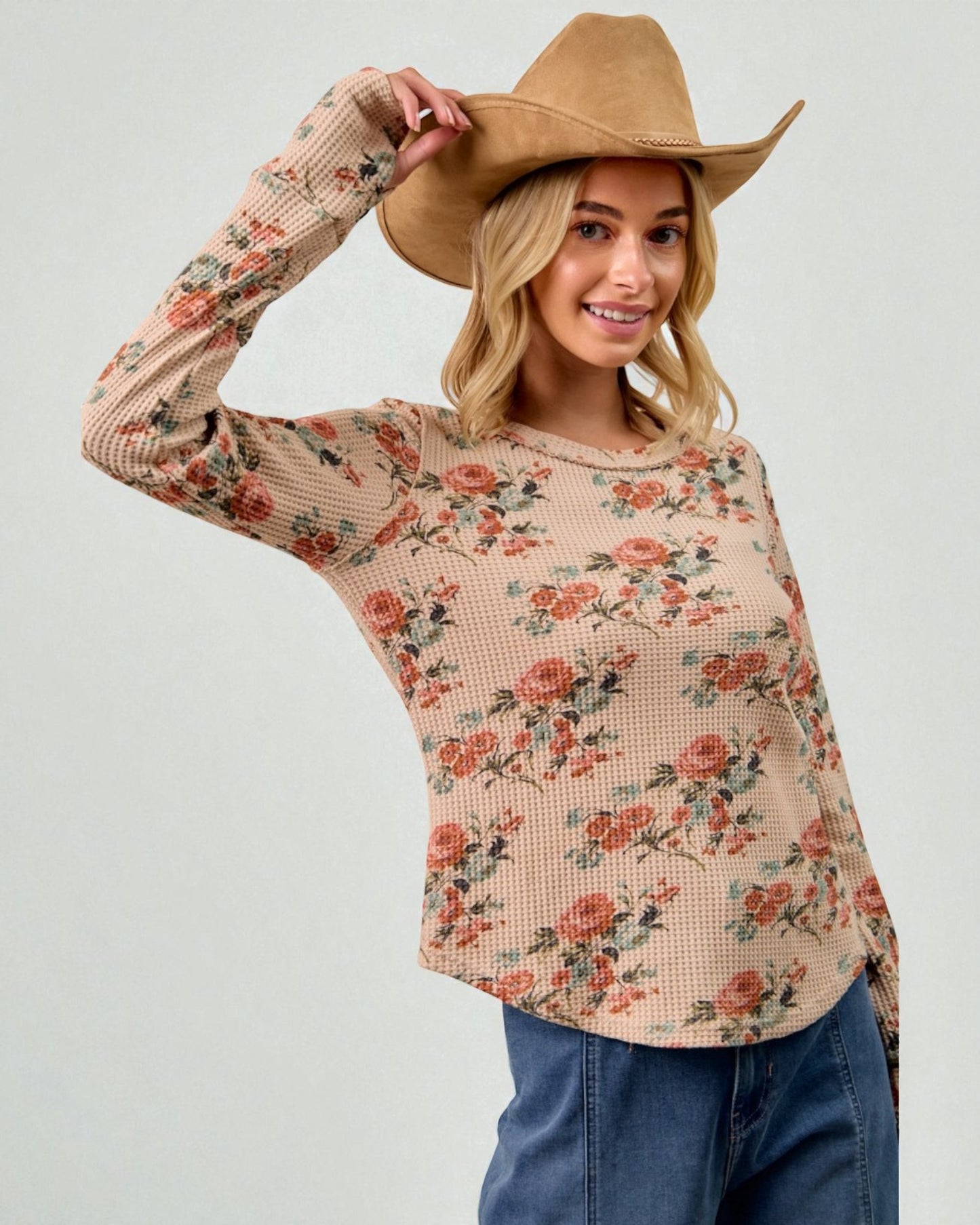 Woman wearing a floral long-sleeve top and a cowboy hat on a plain background