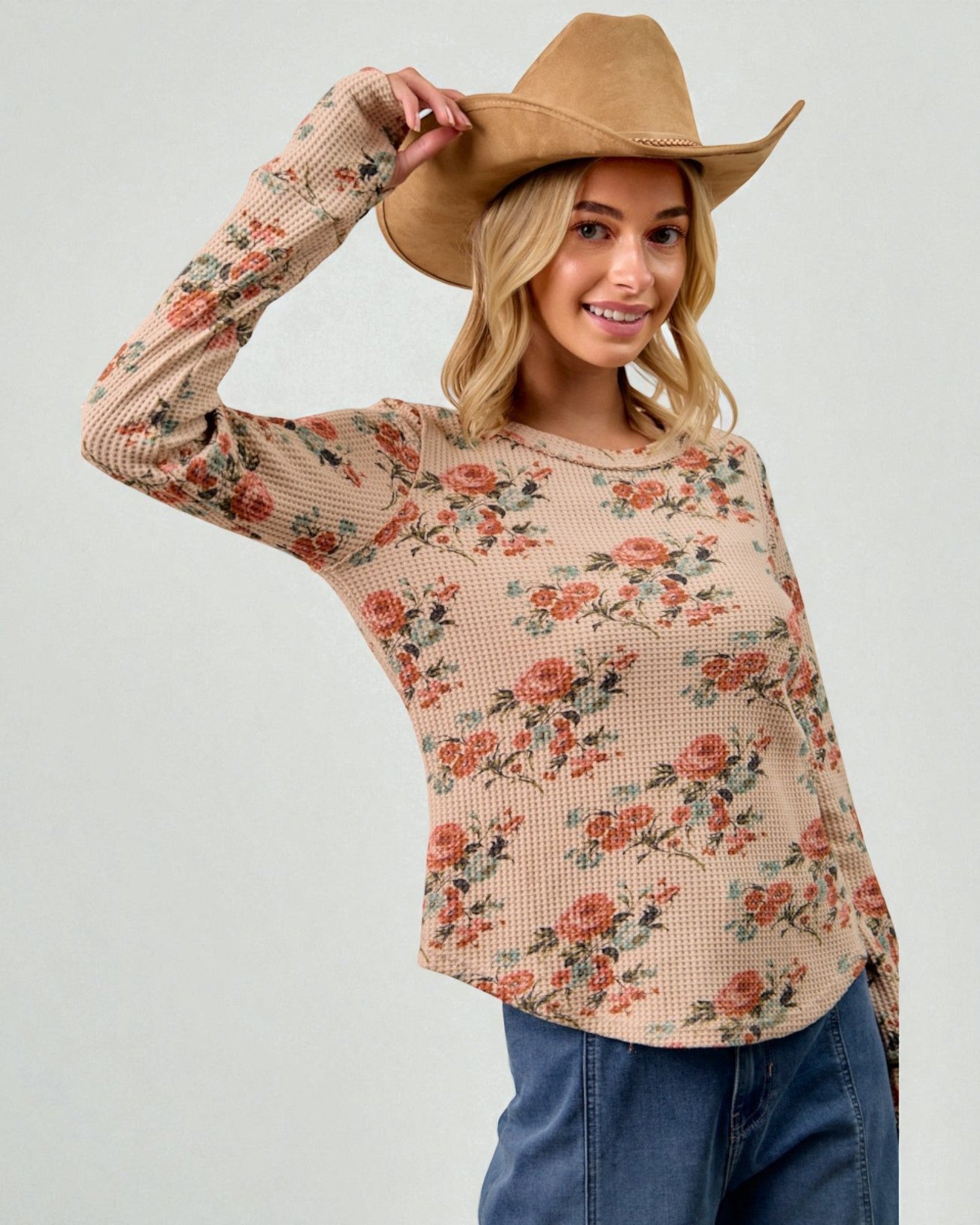 Woman wearing a floral long-sleeve top and a cowboy hat on a plain background