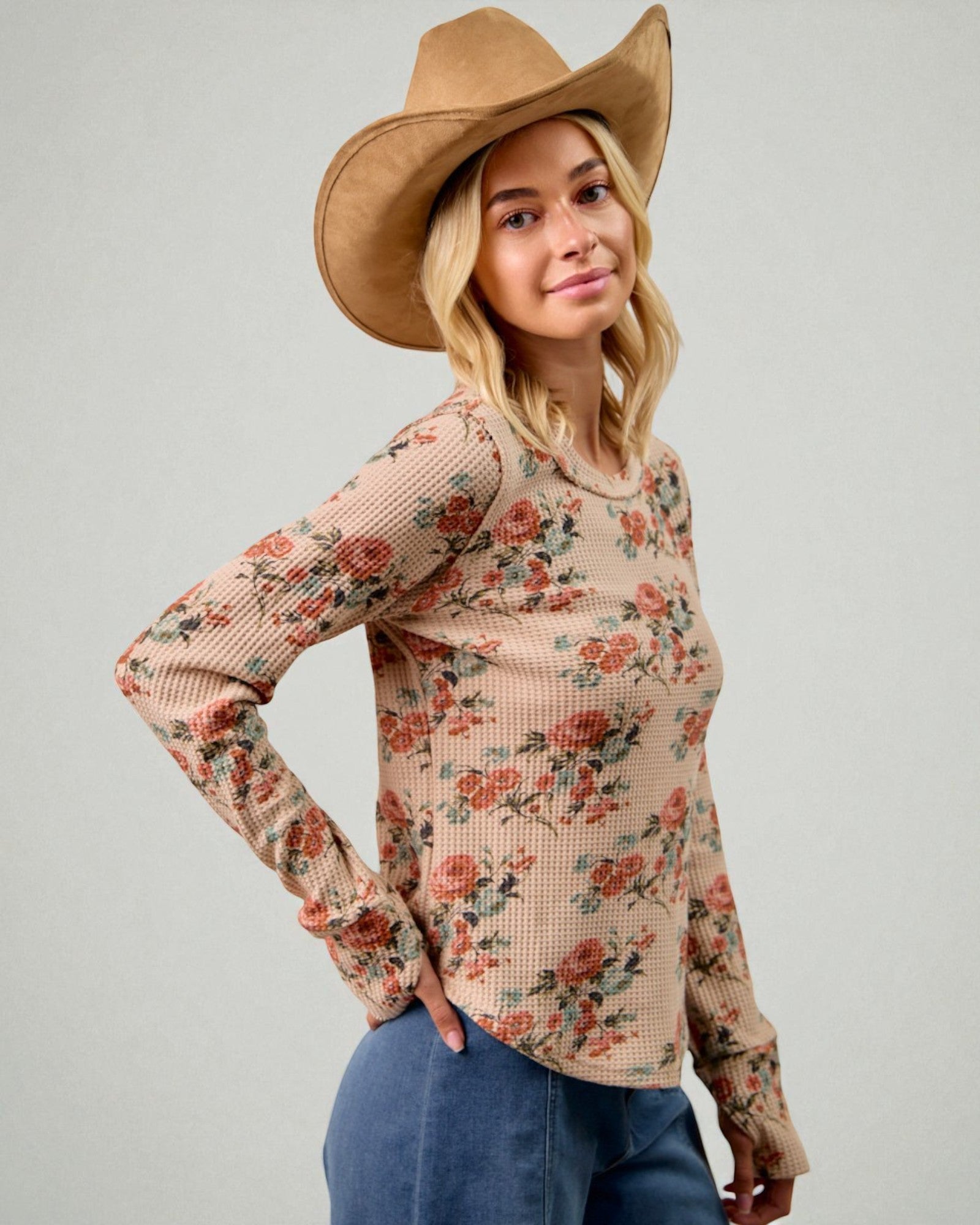 Woman wearing a floral long-sleeve top and wide-brimmed hat against a plain background