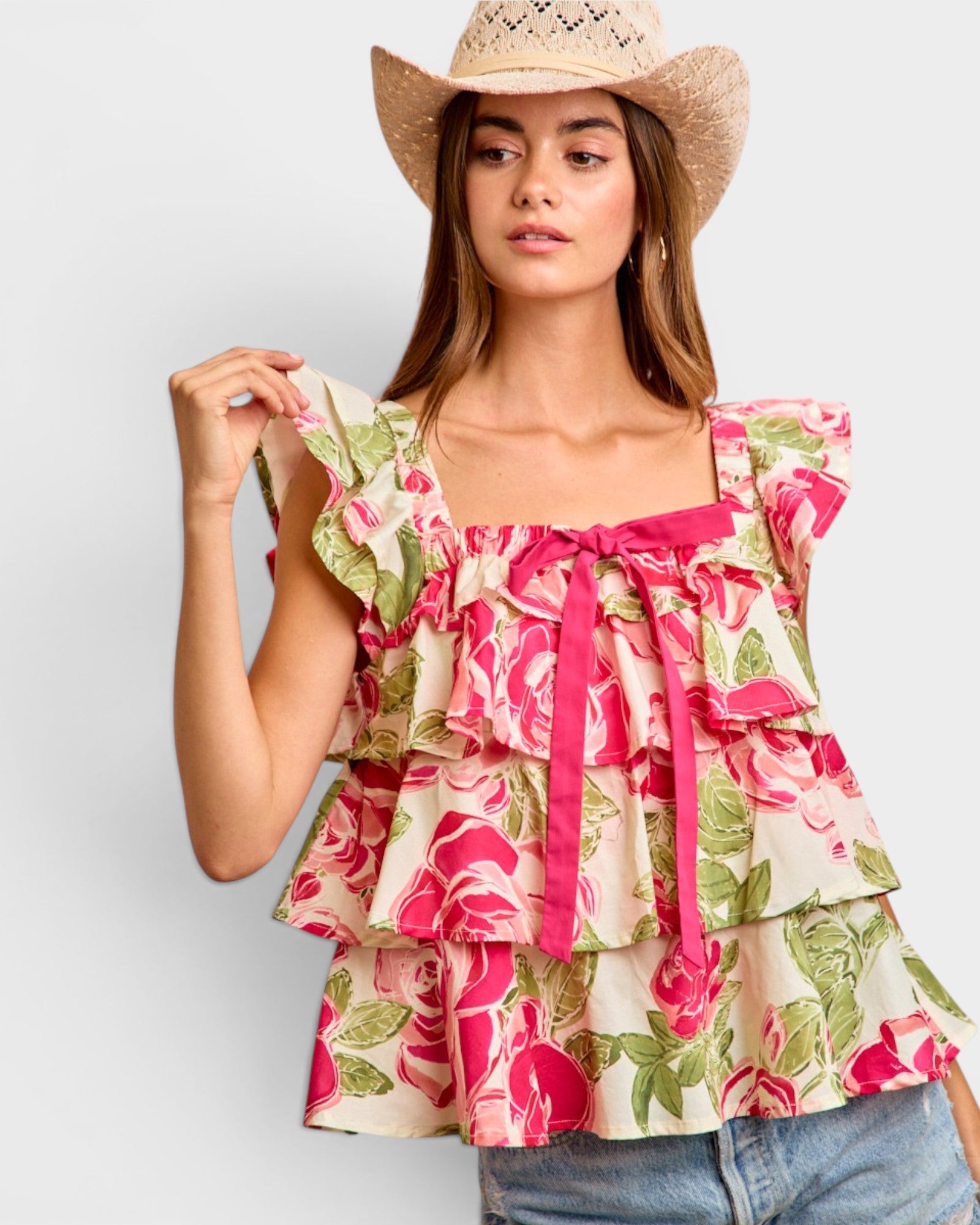 Woman wearing a floral top and cowboy hat on a plain background