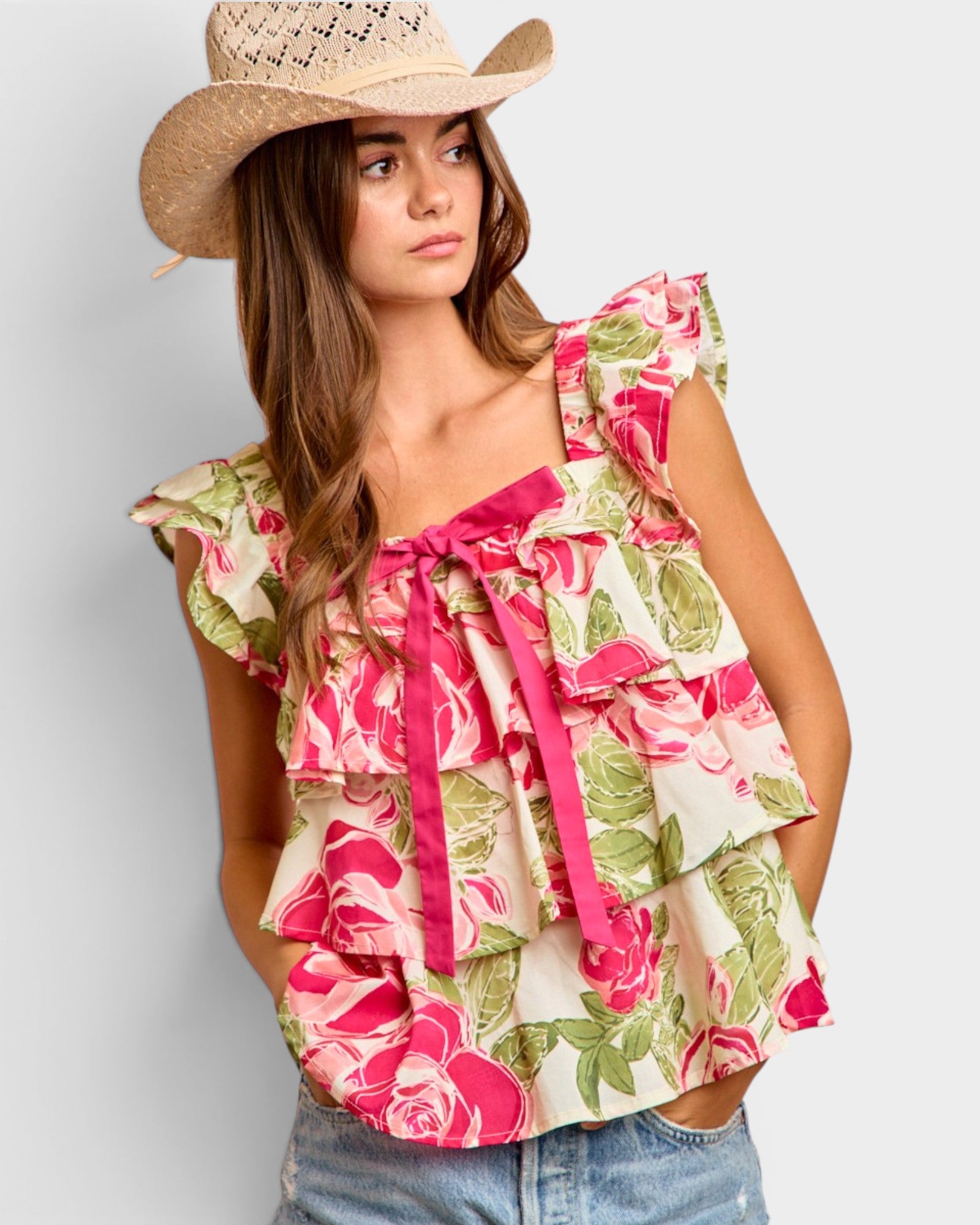 Woman wearing a floral top and cowboy hat against a plain background