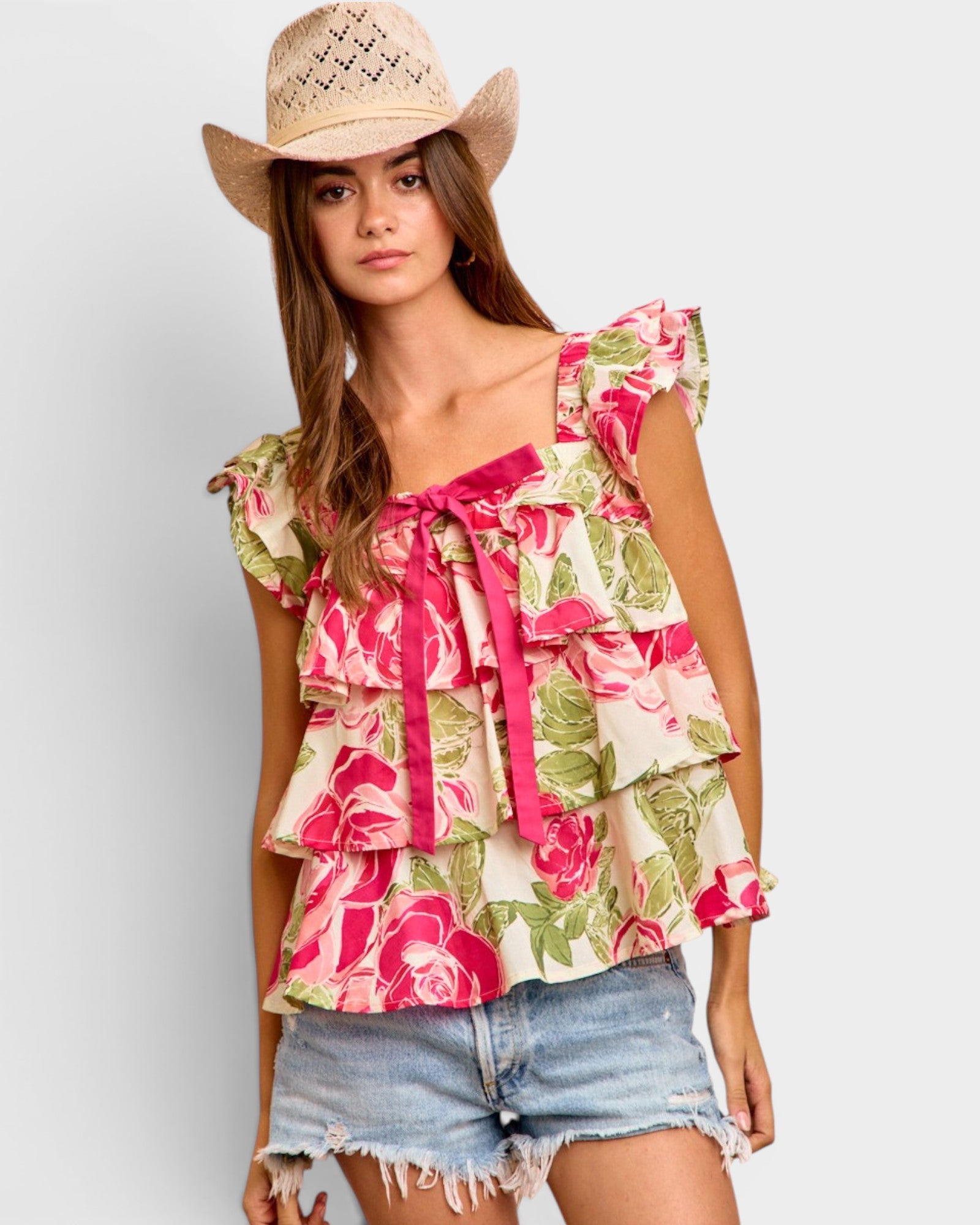 Woman wearing a floral top and denim shorts with a straw hat on a light gray background