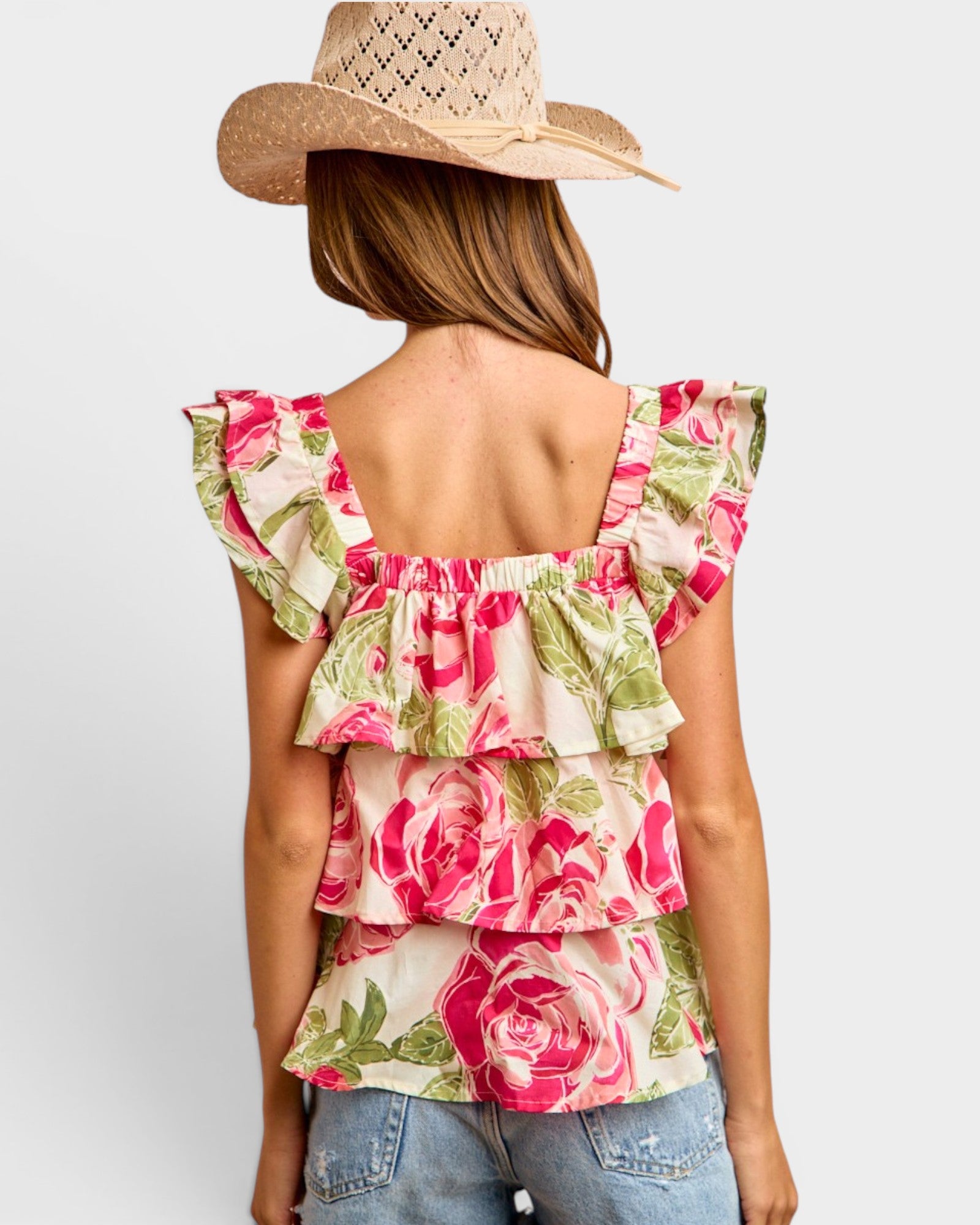 Woman wearing a floral top and straw hat on a plain background