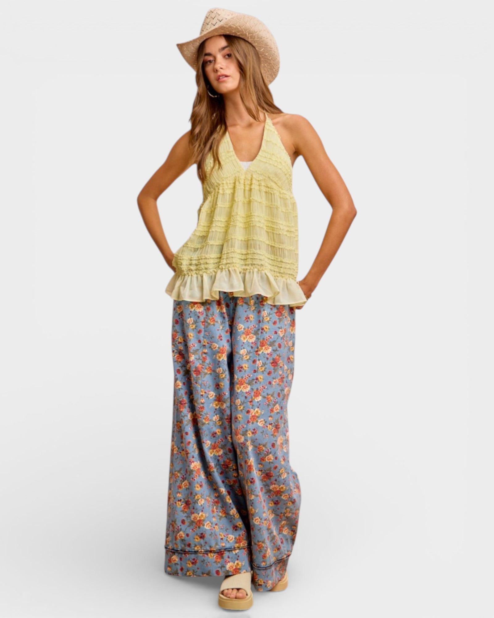 Woman wearing a yellow top and floral pants with a straw hat on a white background