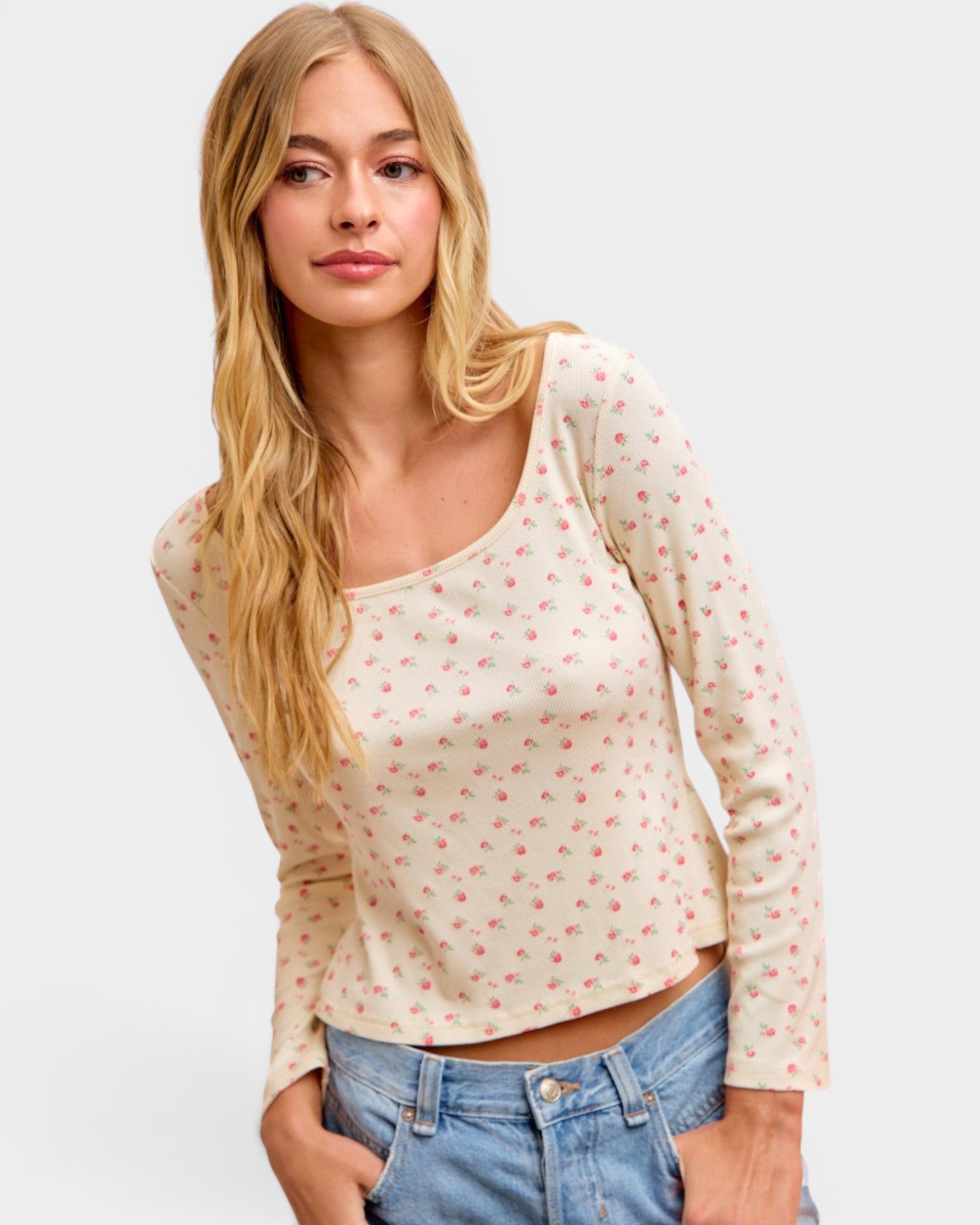 Woman wearing a cream long-sleeve top with red patterns and blue jeans on a light gray background