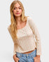 Woman wearing a cream long-sleeve top with red patterns and blue jeans on a light gray background