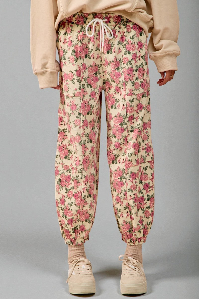 Person wearing floral jogger pants and beige shoes on a gray background