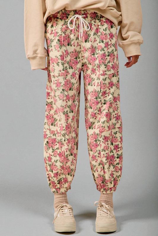 Person wearing floral jogger pants and beige shoes on a gray background