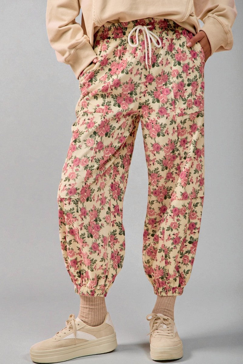 Floral jogger pants worn with a beige sweatshirt and shoes on a gray background