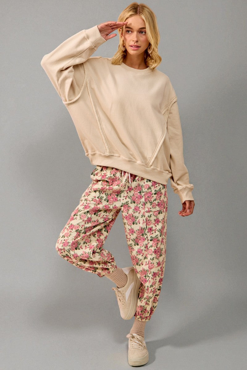 Woman wearing a beige sweatshirt and floral pants against a gray background