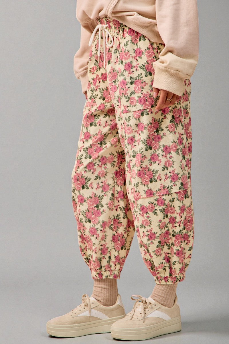 Floral pants worn with a light pink sweatshirt and white sneakers on a gray background
