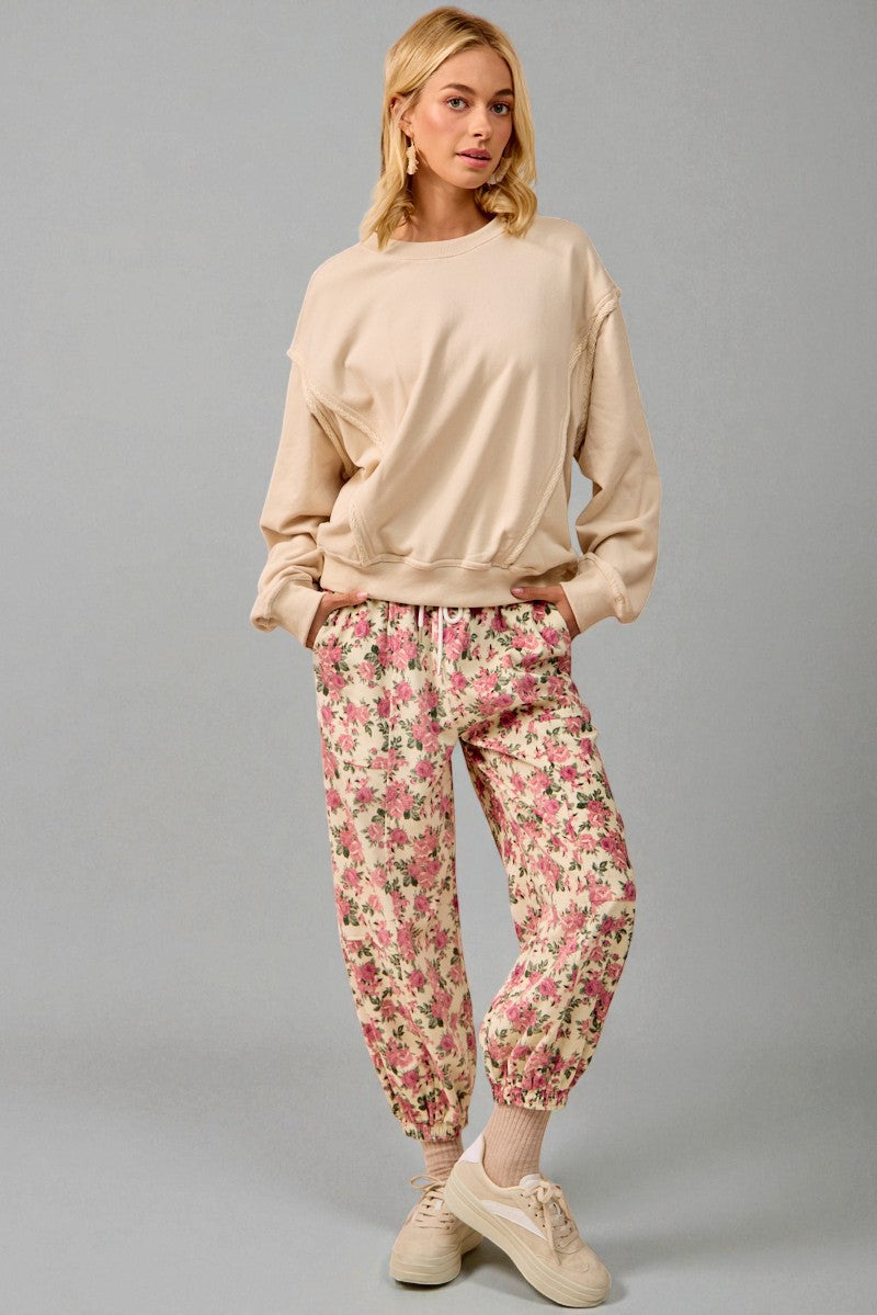 Woman wearing a beige sweatshirt and floral pants on a gray background
