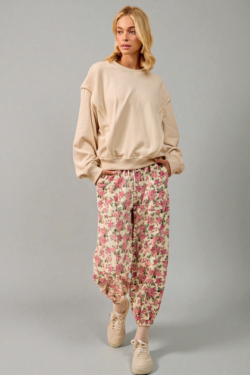 Woman wearing a beige sweatshirt and floral pants on a gray background